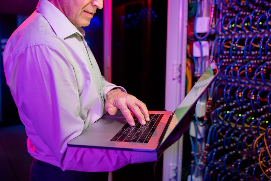 A security system engineer on a laptop identifies a problem near servers